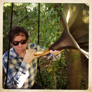 Photo of Grant-Lee Phillips blowing on a a Victrola horn.
